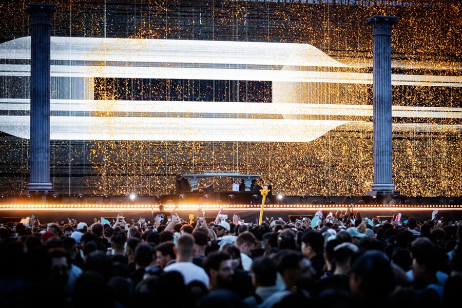 Golden particle visuals fill the main stage screen above a packed crowd