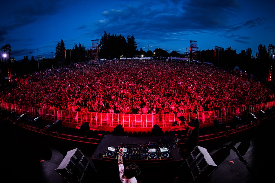 The Soul Rise crowd bathed in red light at dusk, seen from behind the decks, with the Lions Gate Bridge on the horizon